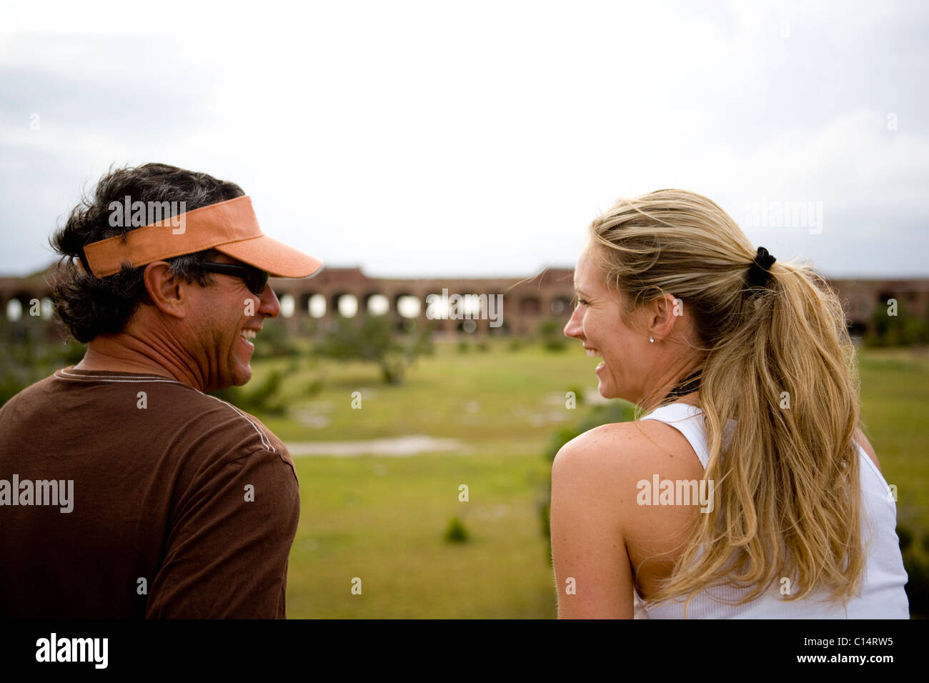 A man and a woman look at each other and laugh with grass and an old brick structure in the background. Stock Photo