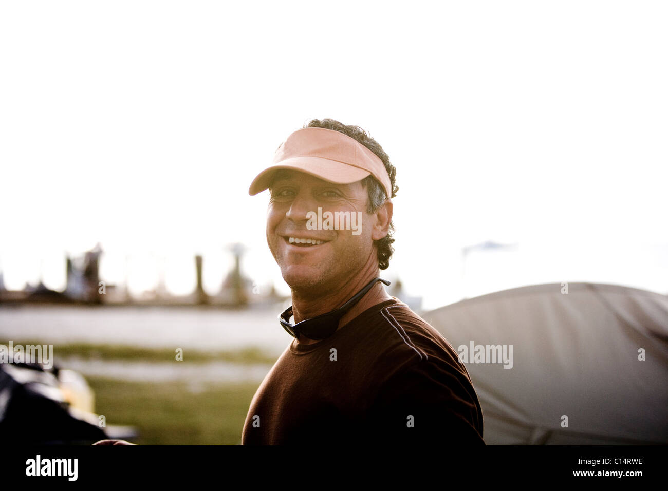 A man in an orange visor with sunglasses softly smiles at the camera. Stock Photo