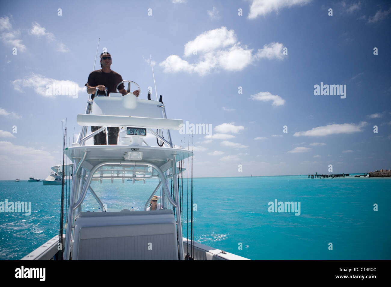 A fisherman steers his boat from the fly bridge negotiating blue-green tropical waters. Stock Photo