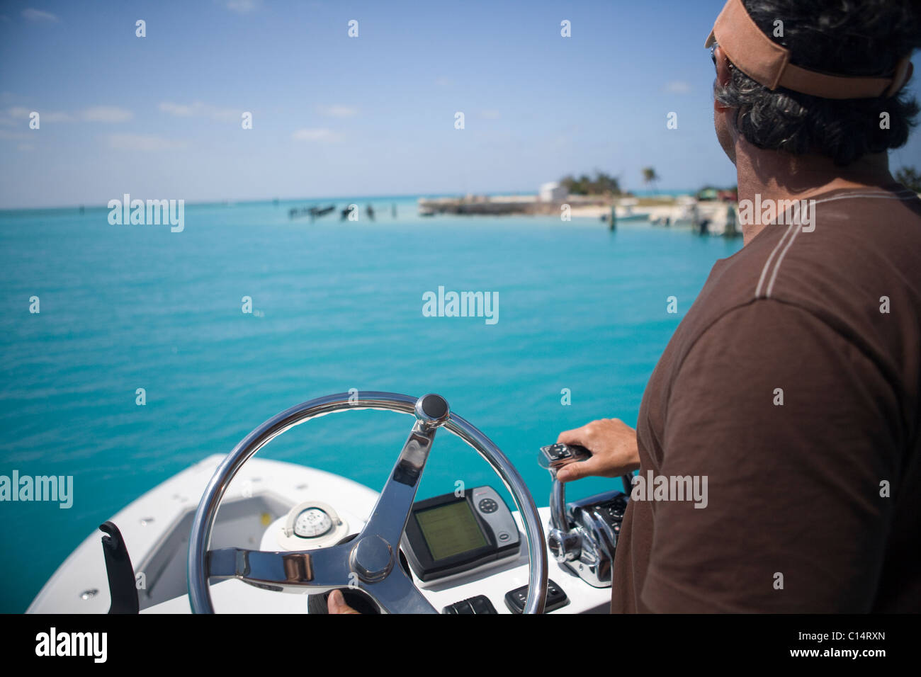 A fisherman steers his boat and hits the throttle from the fly bridge as he gazes out at the blue-green tropical waters. Stock Photo