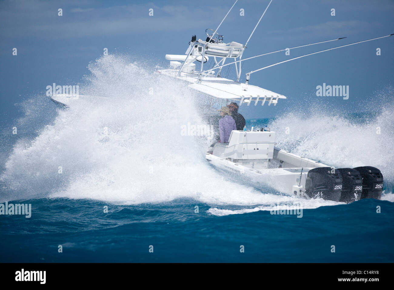 A fishing boat speeds through the blue surf spraying white water. Stock Photo