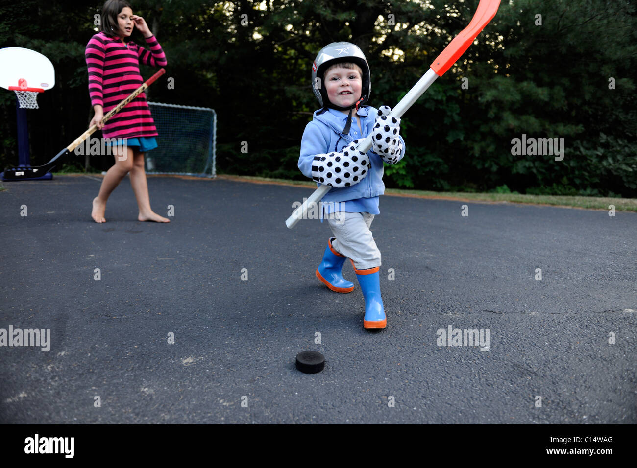 2 year old causcasian boy and his 10 year old caucasian girl cousin play street hockey Stock Photo
