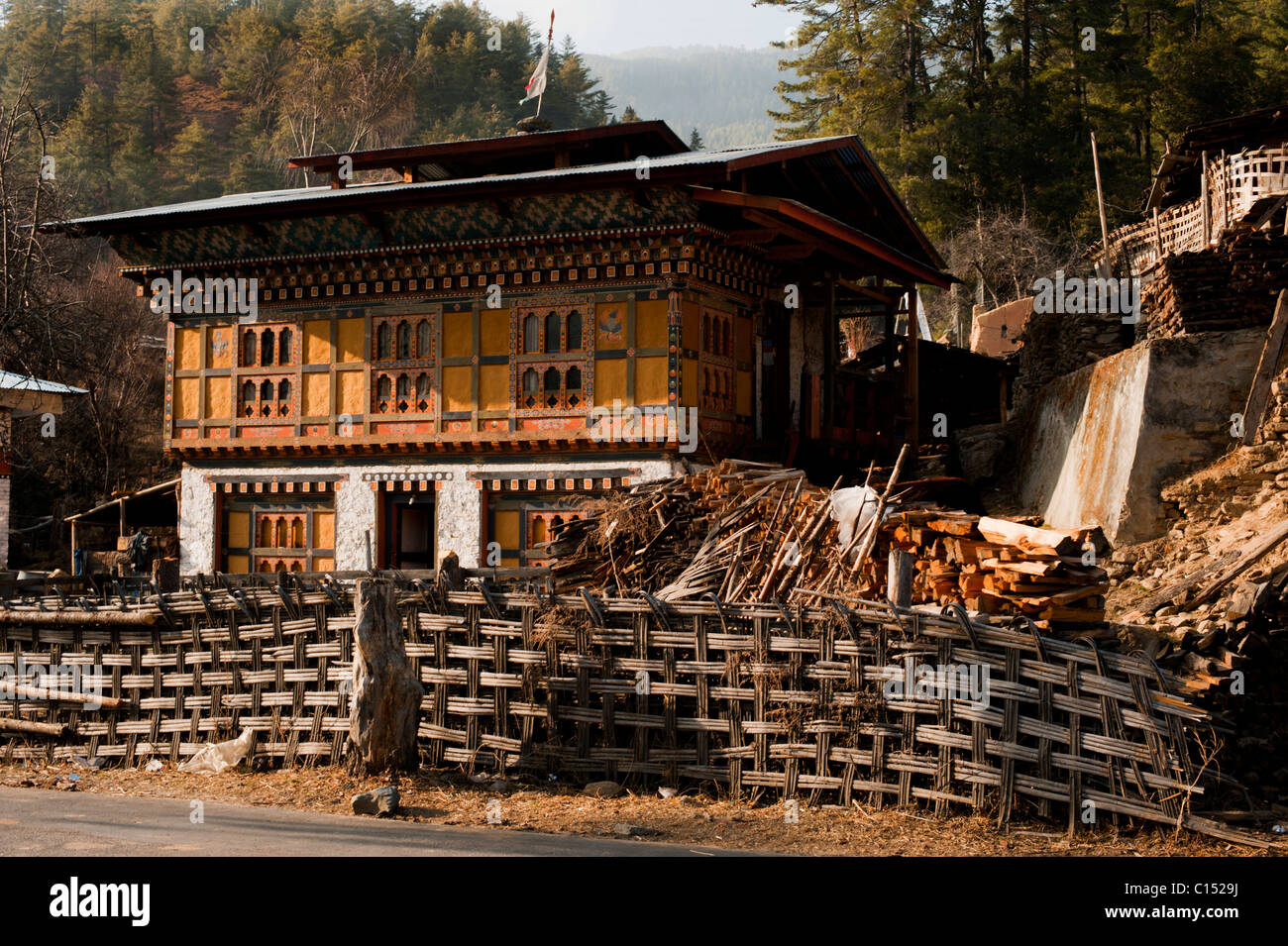 Traditional Bhutanese house in rural Bhutan with wooden details and traditonal bamboo fence. Stock Photo