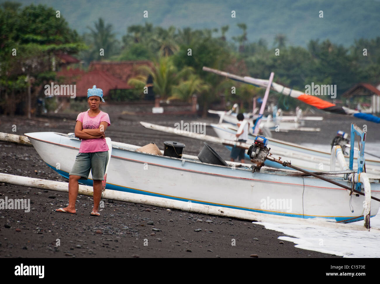 A Balinese woman waits on the beach for her husbands'  fishing boat to come in after a nights fishing for mackerel in Amed, Bali Stock Photo