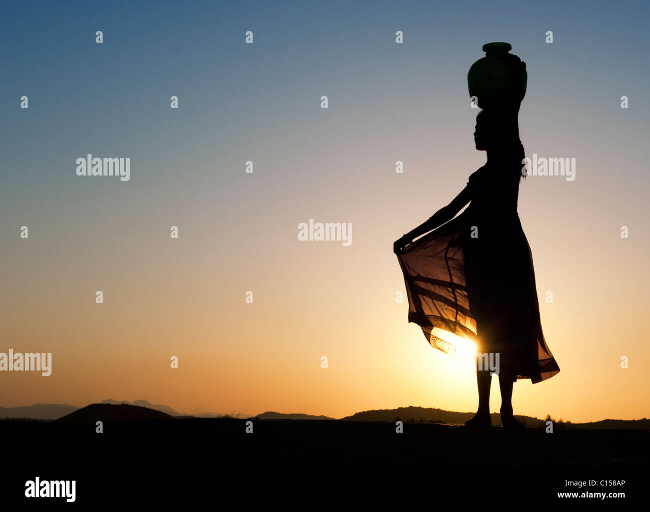 Rural Indian village girl balancing a water pot on her head at sunset. Silhouette. Andhra Pradesh, India Stock Photo