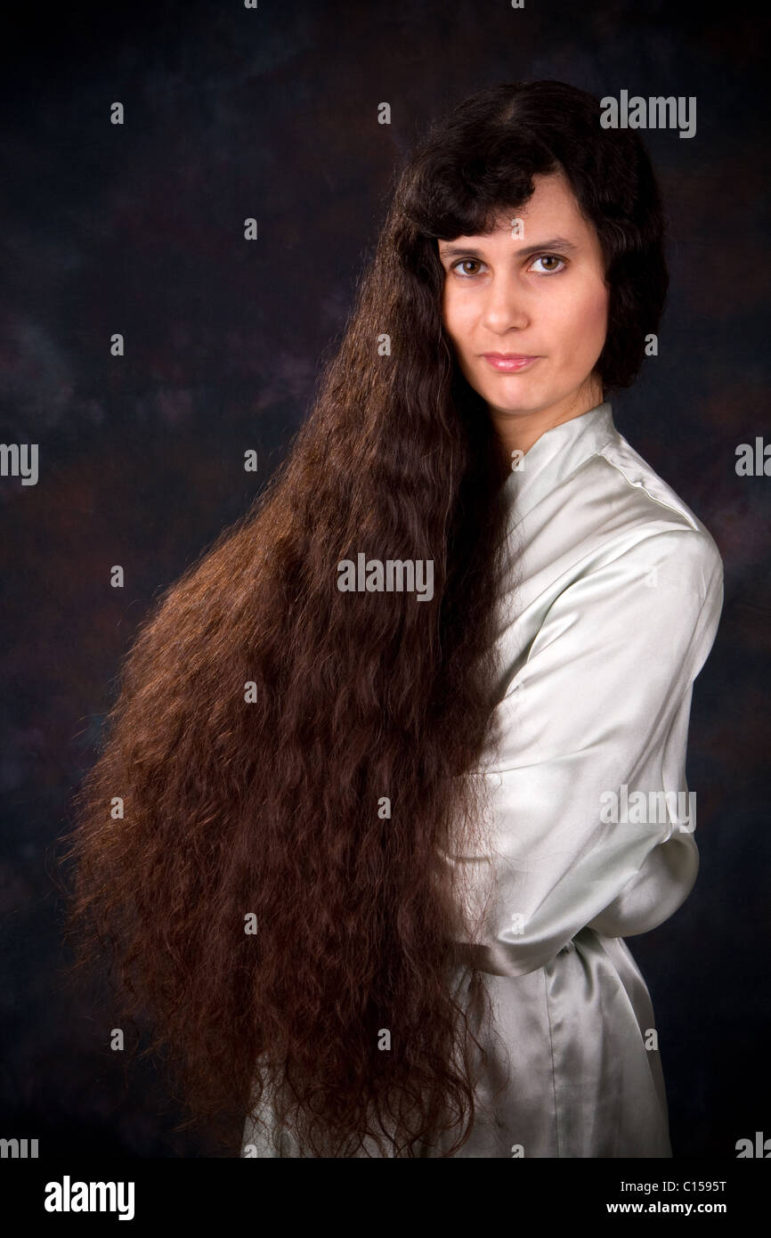 Extremely long haired Middle Eastern woman in a light blue robe poses in front of a dark background. Stock Photo
