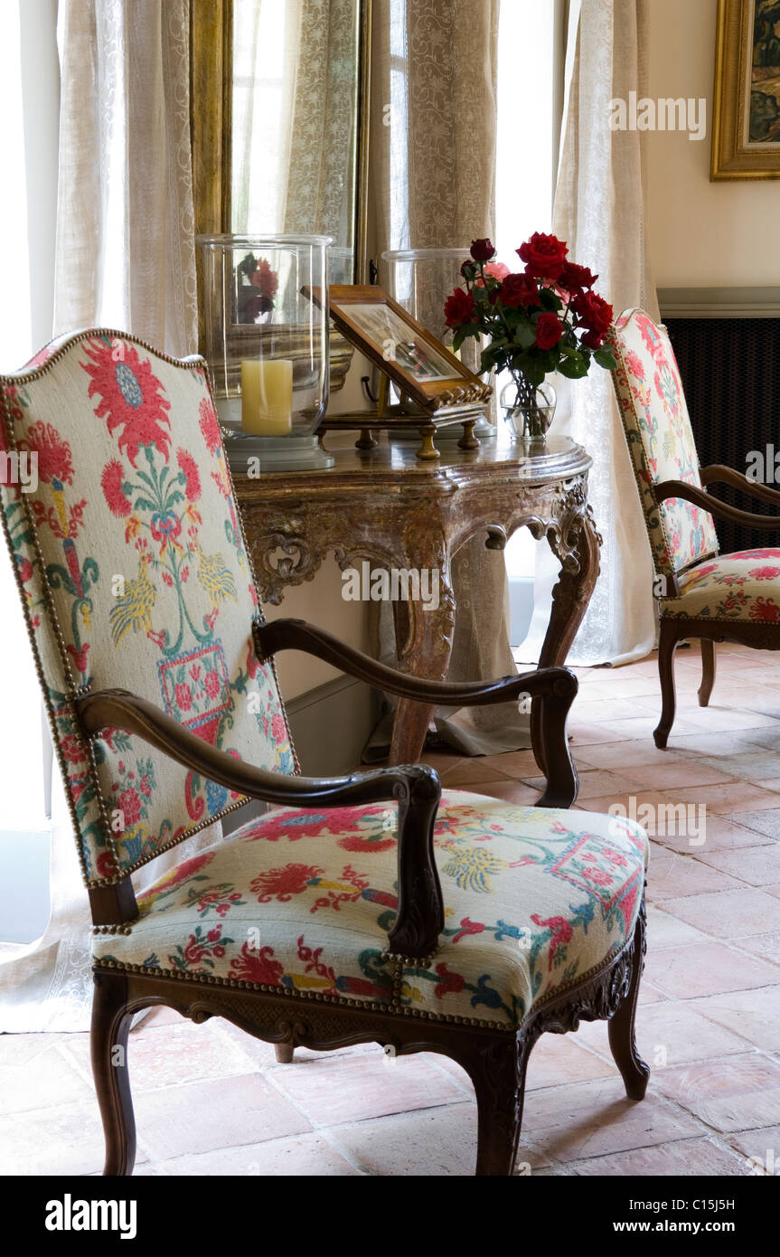 High back armchair upholstered in floral textile in room with  gilt french console table and terracotta flooring Stock Photo