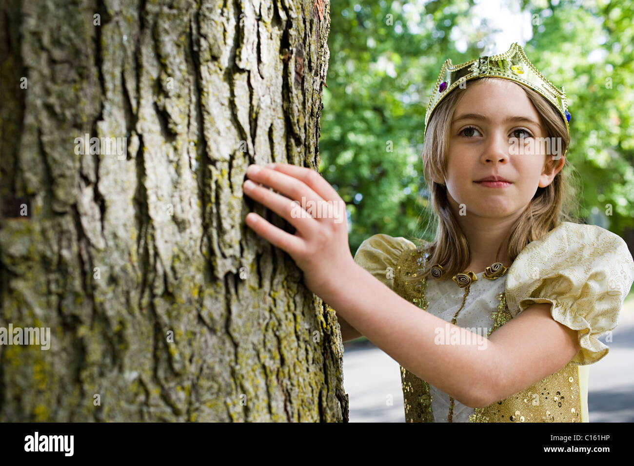 Girl dressed up as queen touching tree trunk Stock Photo Alamy