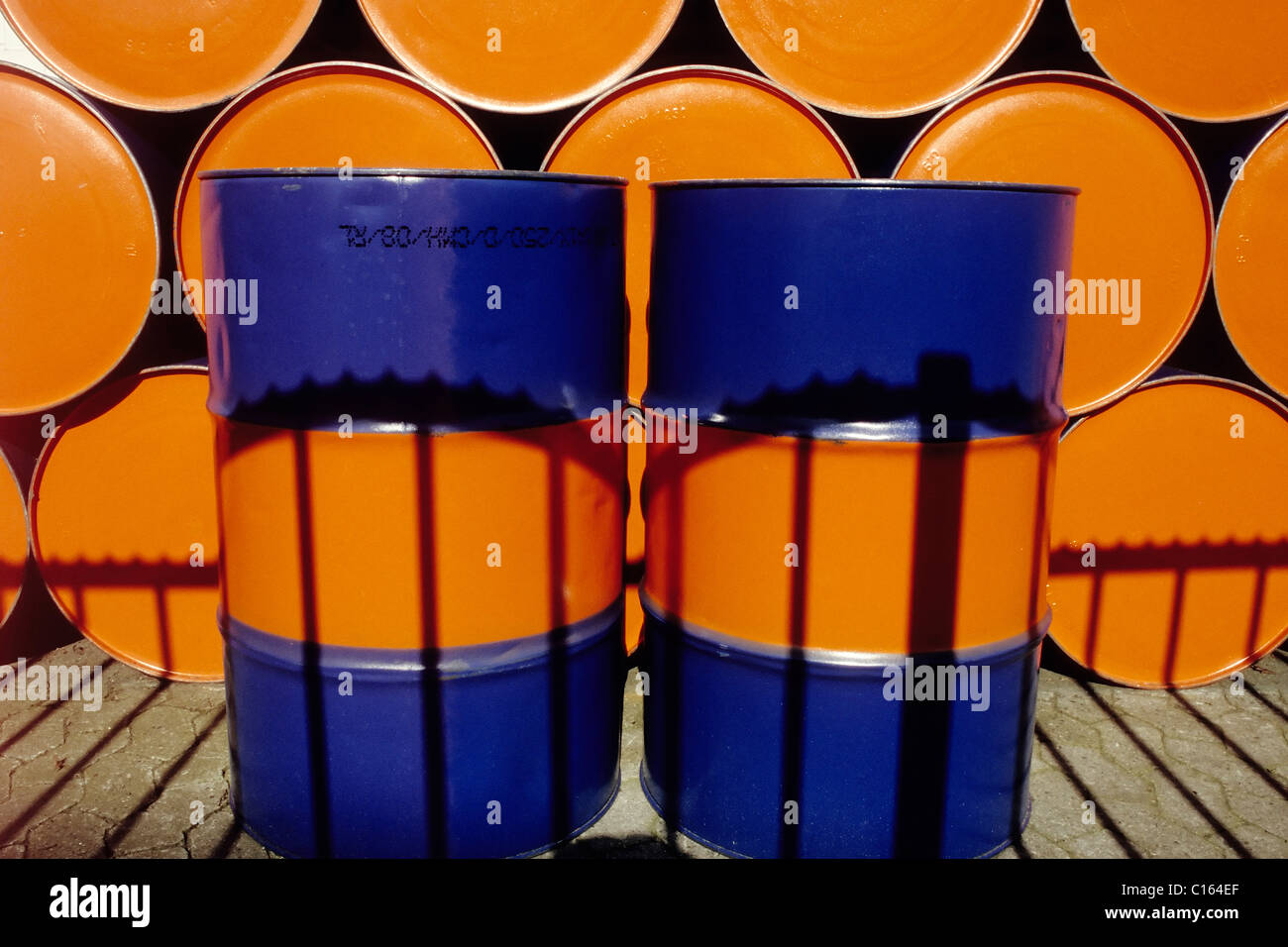 Two upright oil drums painted two colors standing in front of a row of stacked oil drums Stock Photo