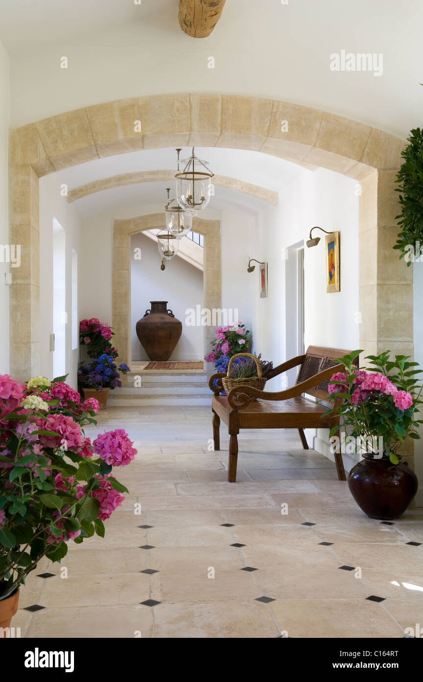 Stone arched corridor with potted hydrangeas and wooden armchair Stock Photo