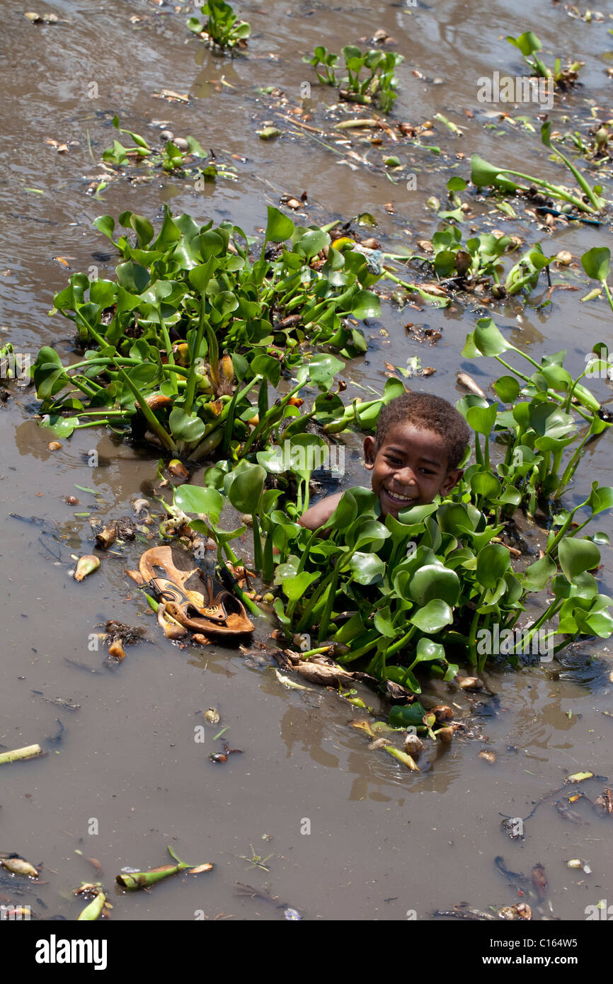 Malagasy Boy helping gather introduced and invasive Water Hyacinth (Eichhornia crasspipes). Madagascar. Stock Photo