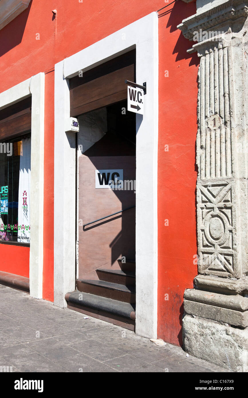 opening in vibrant red plaster wall with stairway access to public WC restrooms on a street in Oaxaca de Jaurez Mexico Stock Photo