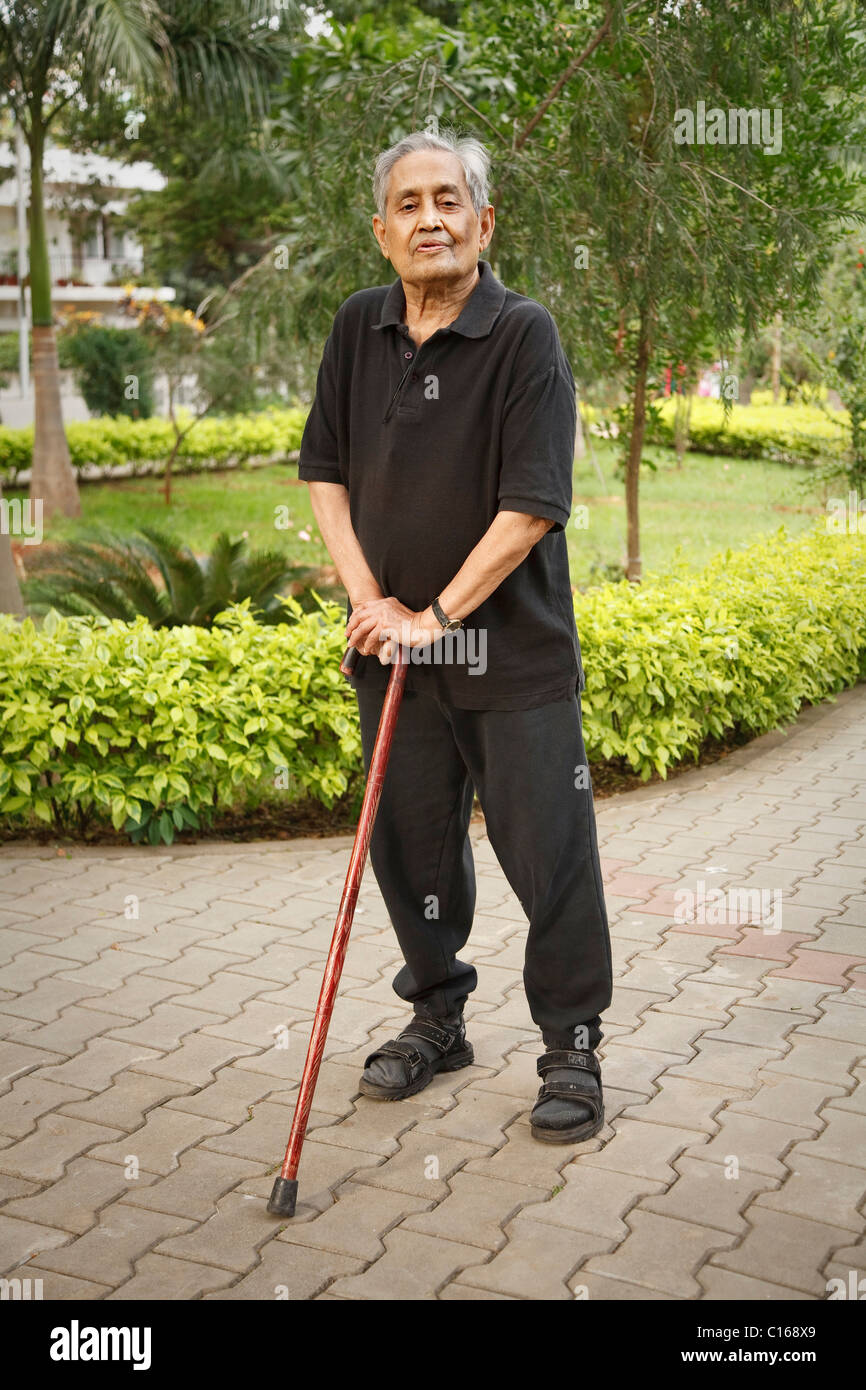 Old Indian Asian man stands in a park with a walking stick Stock Photo