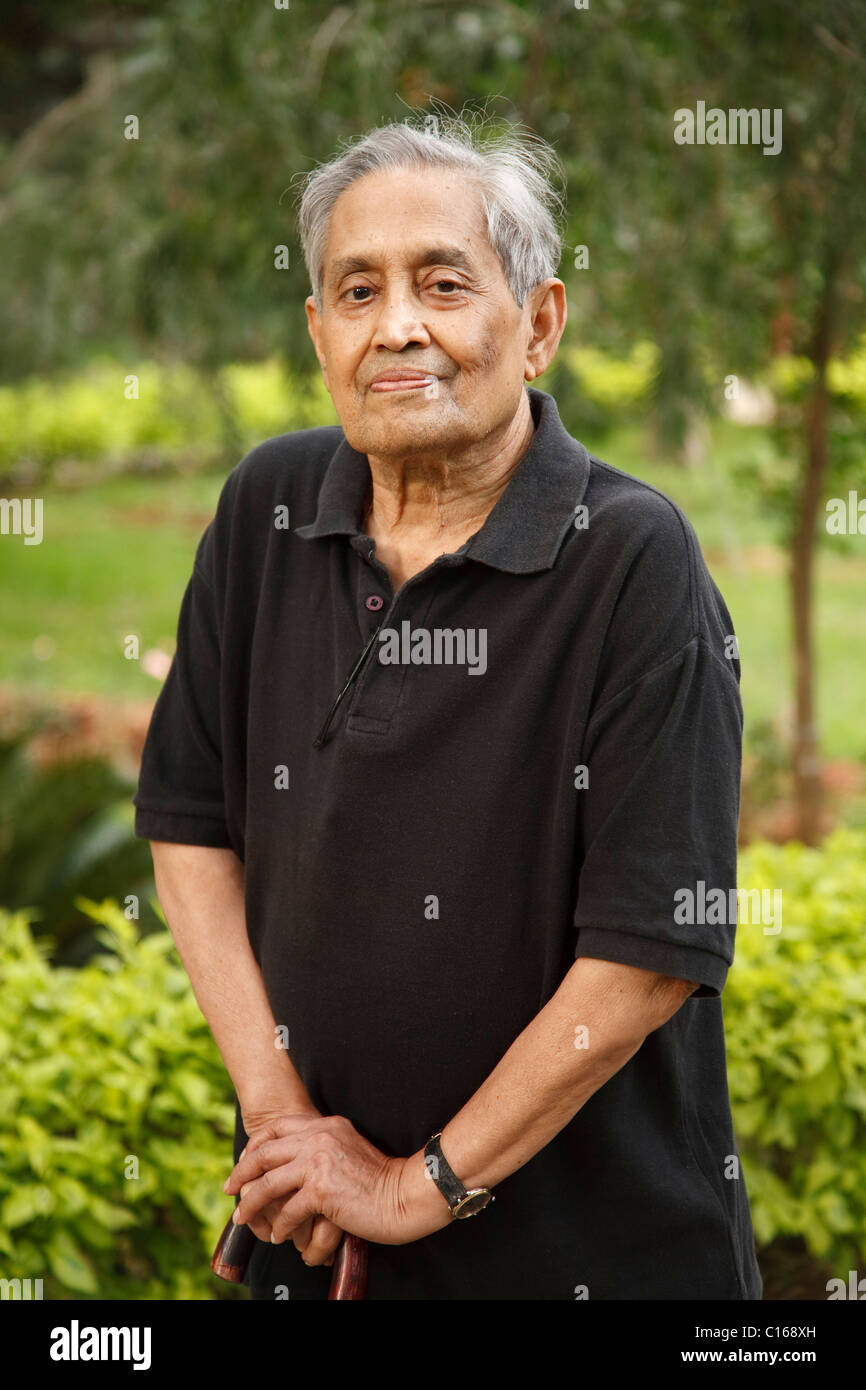 Elderly Indian Asian man stands in a park with a walking stick Stock Photo