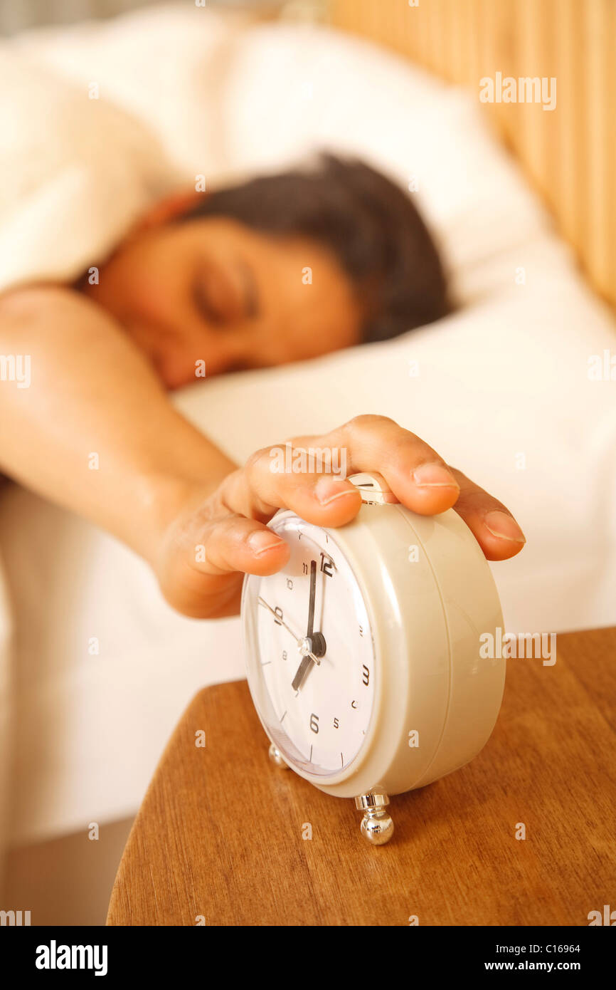 An Indian Asian woman wakes up to turn off a traditional alarm clock Stock Photo