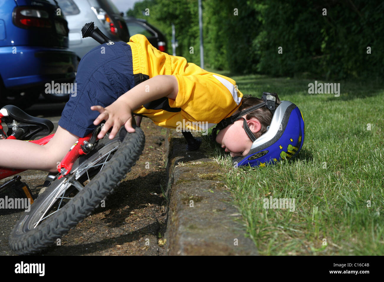 Five-year-old boy wearing a bicycle helmet falling off his bicycle, posed photo Stock Photo