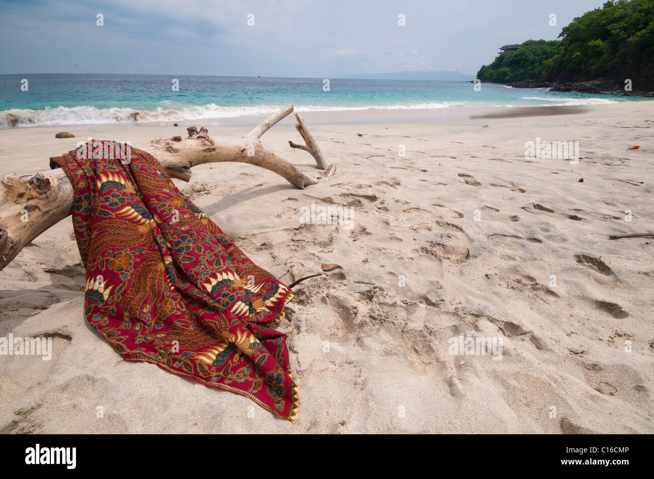A batik sarong draped over driftwood log on the beach at Bias Tegal in Padang Bai Bali Indonesia Stock Photo