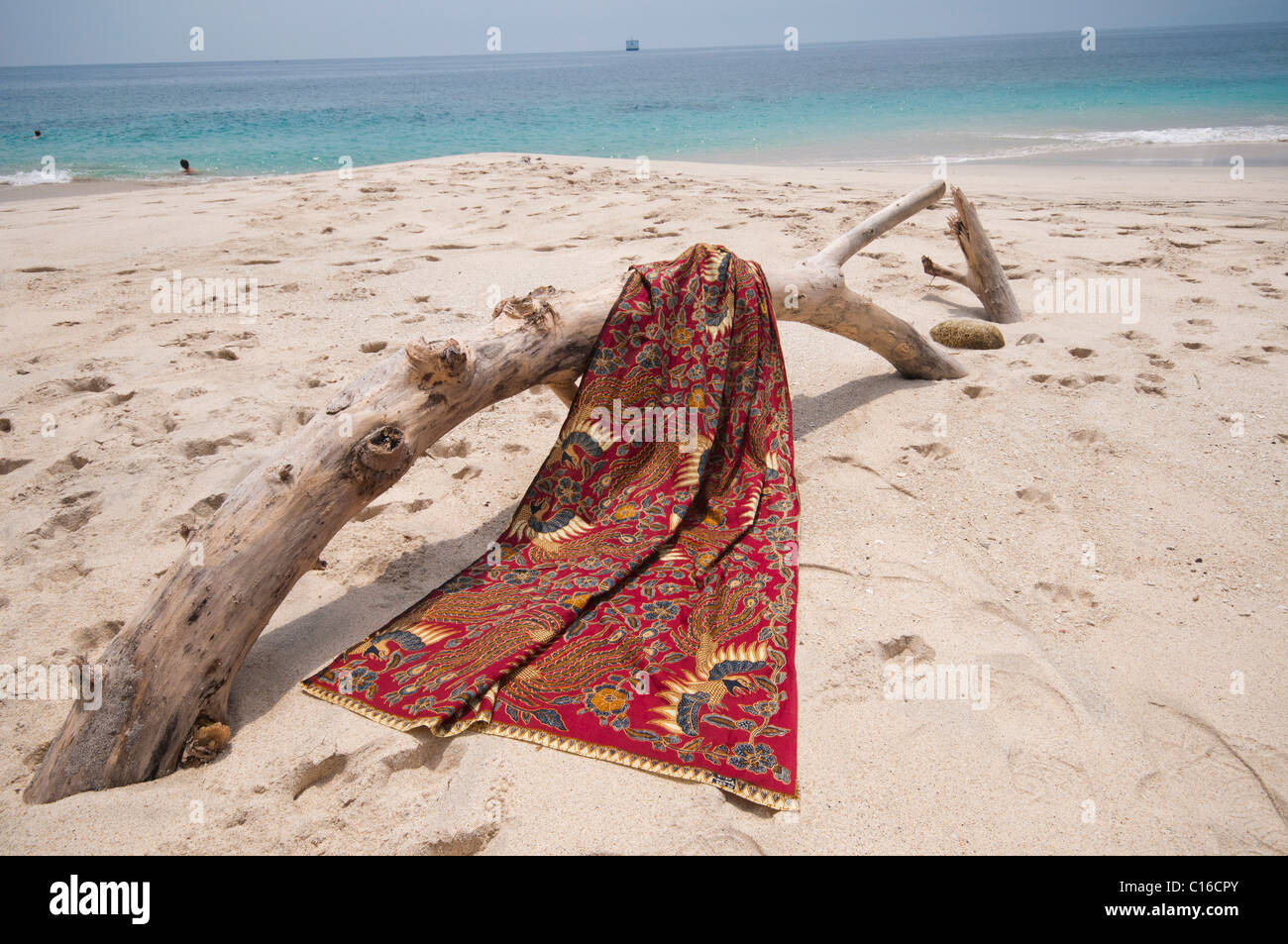 A batik sarong draped over driftwood log on the beach at Bias Tegal in Padang Bai Bali Indonesia Stock Photo
