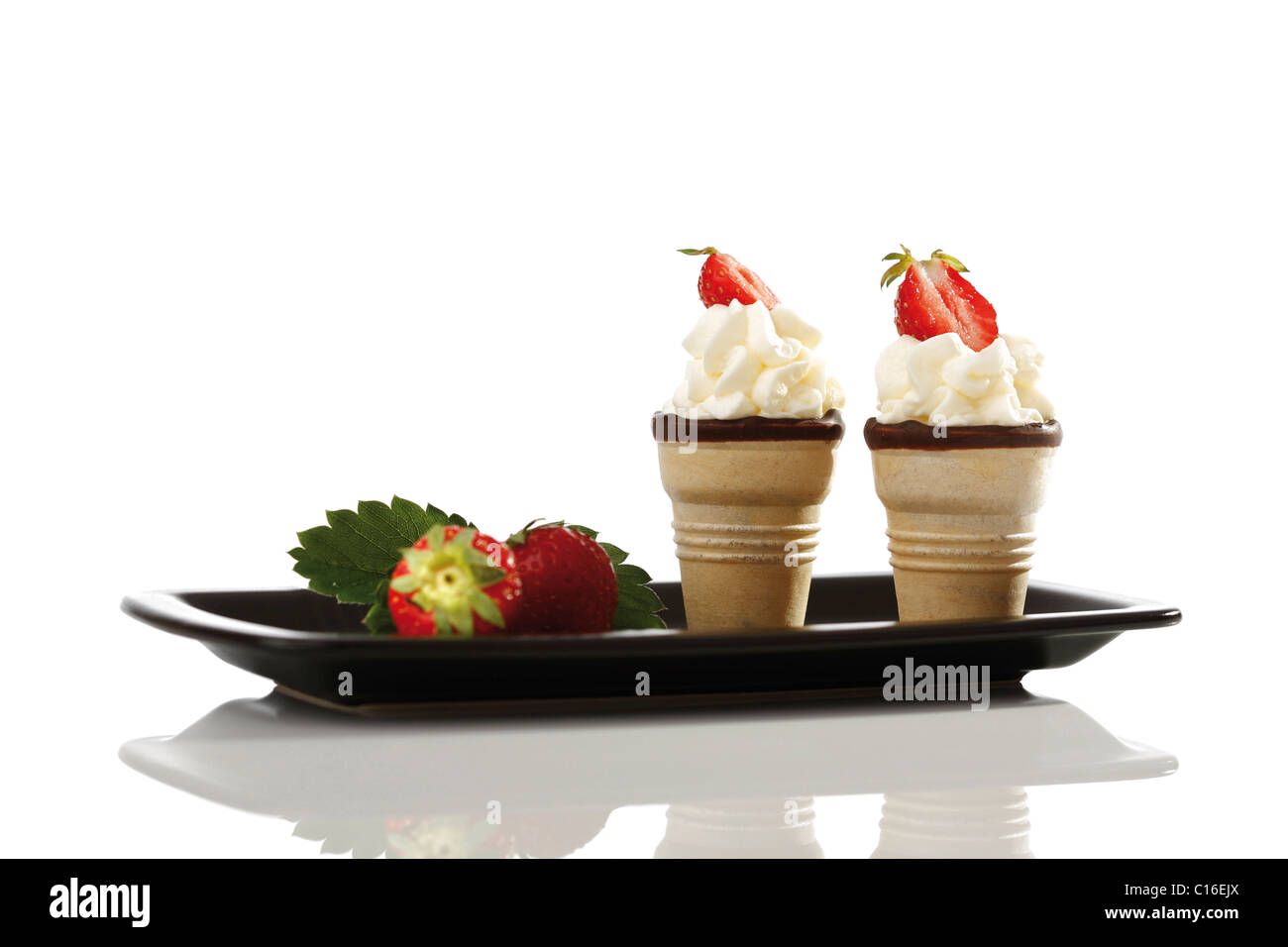 Two wafer cones with cream and strawberries in a black tray Stock Photo