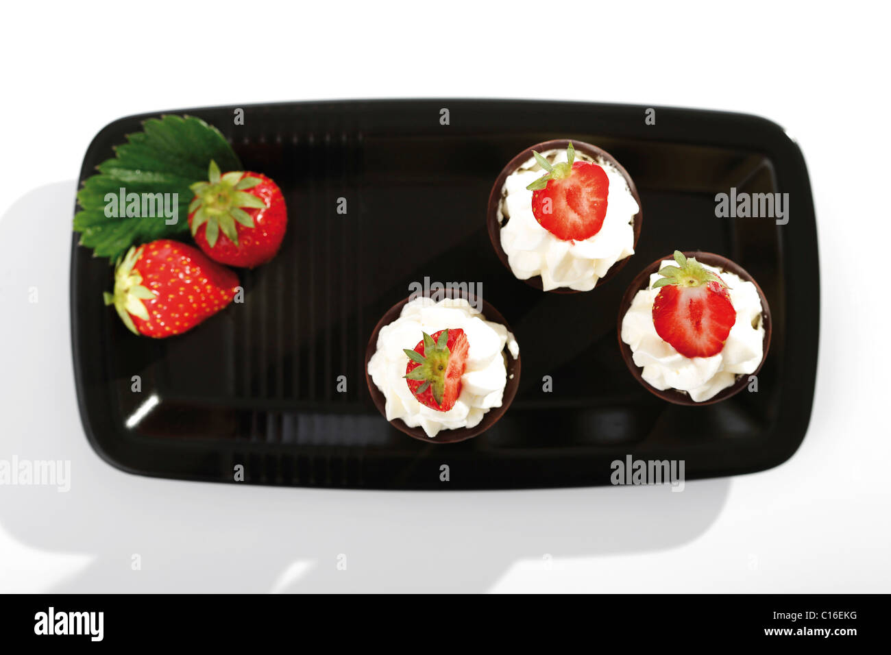 Three wafer cones with cream and strawberries on a black tray Stock Photo