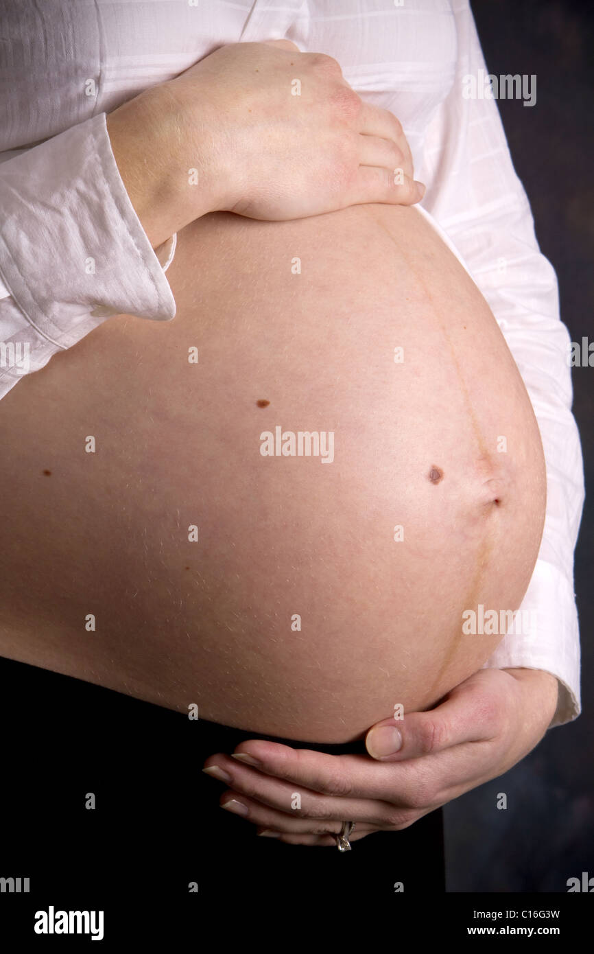 Pregnant woman's abdomen shows a vertical dark line called the linea negra caused by increases in estrogen and progesterone. Stock Photo