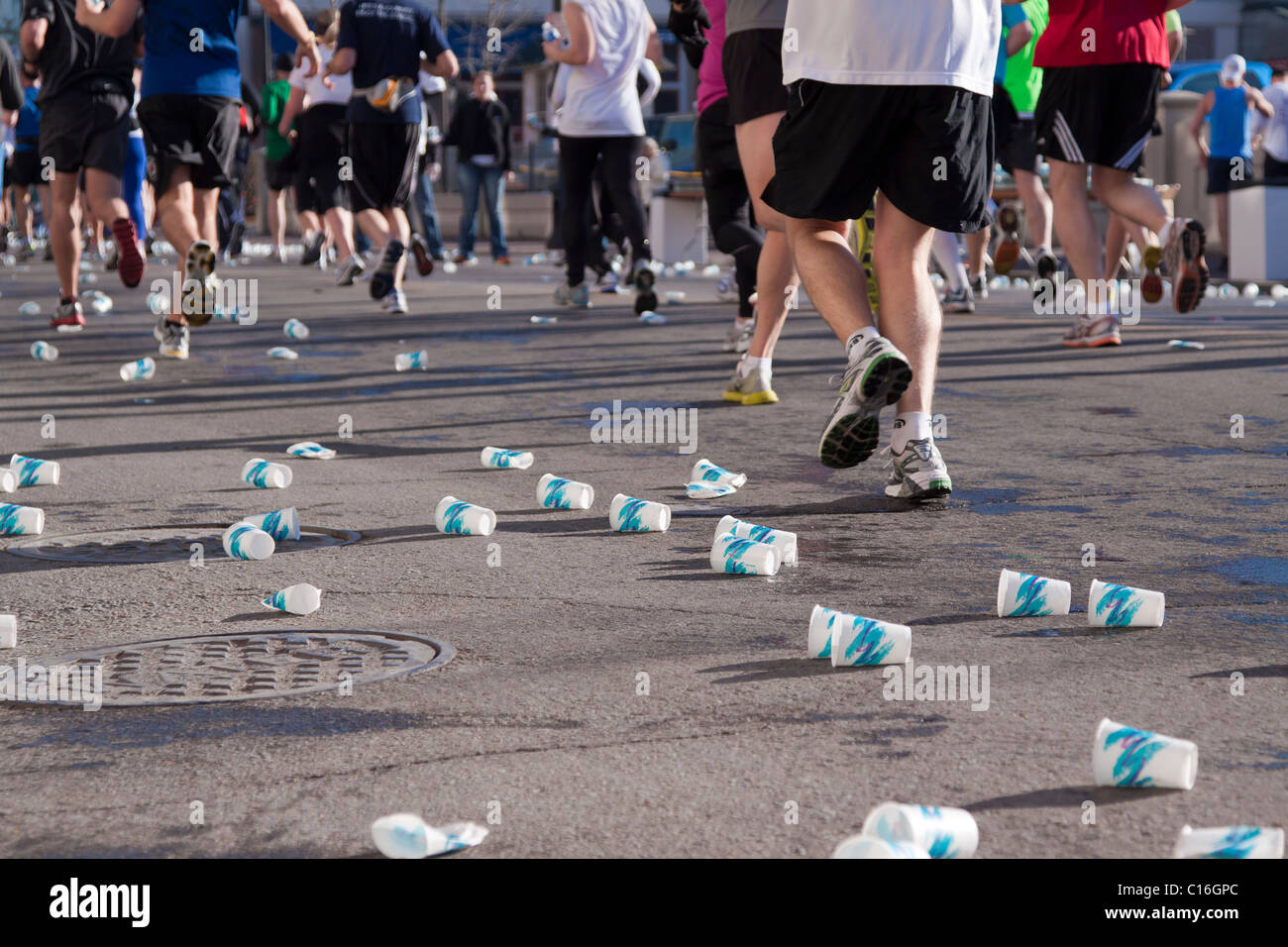 Legs and feet of marathon runners as they run by a water station with paper cups discarded on the ground Stock Photo