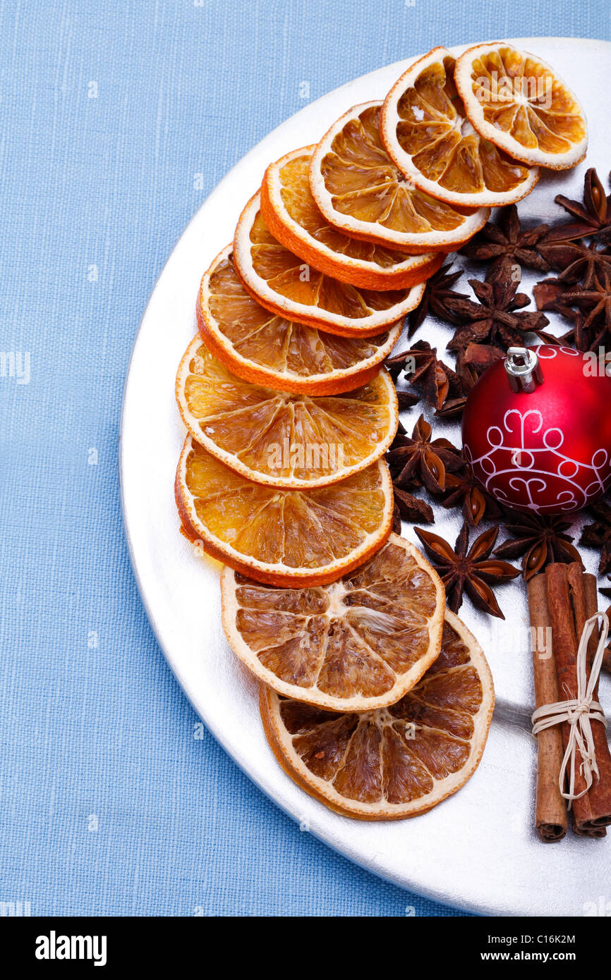Dried slices of orange, star anise, Christmas bauble and cinnamon sticks on a plate Stock Photo