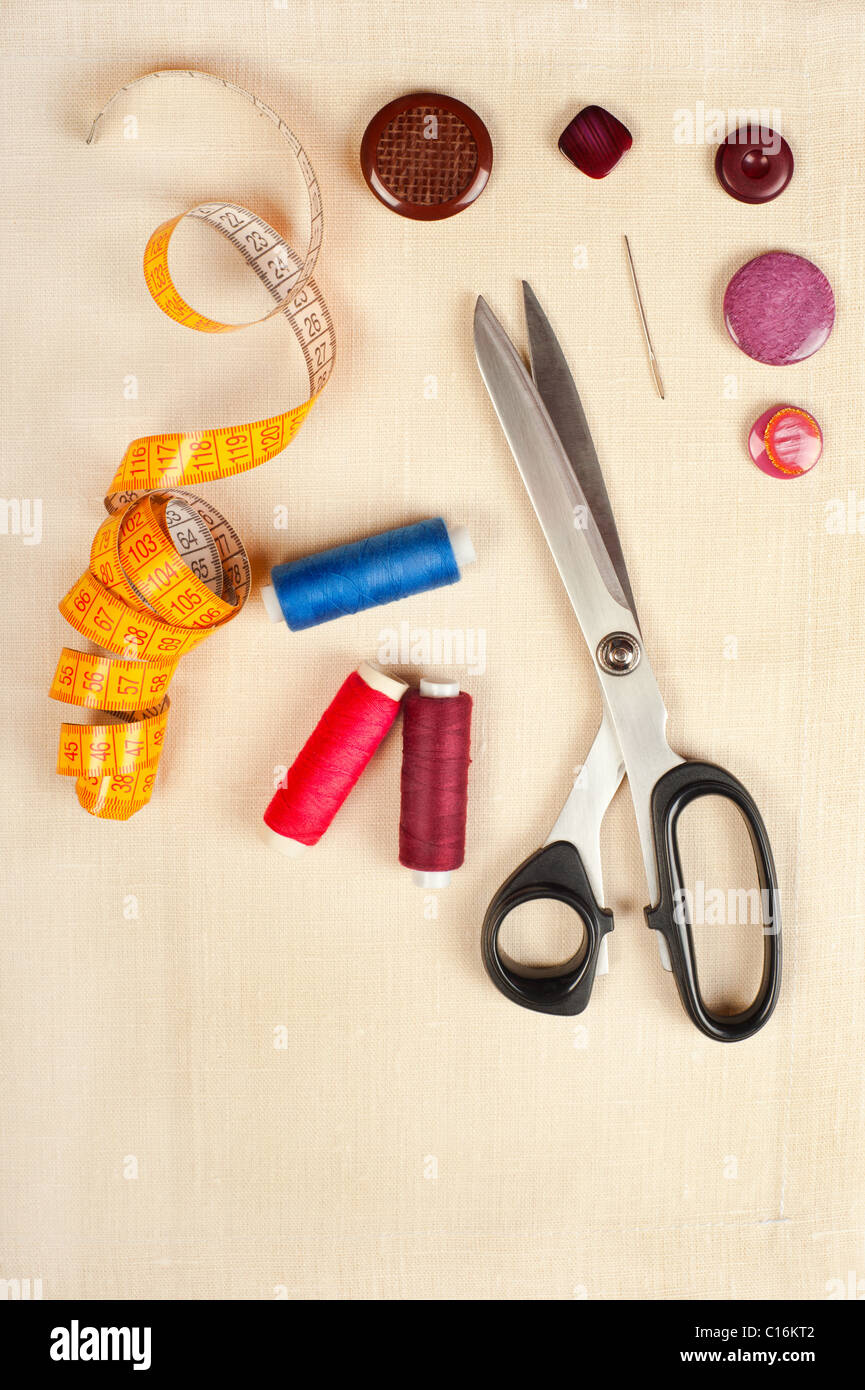 Sewing supplies. Set from measuring tape, buttons, bobbins of thread, needle and scissors on linen Stock Photo