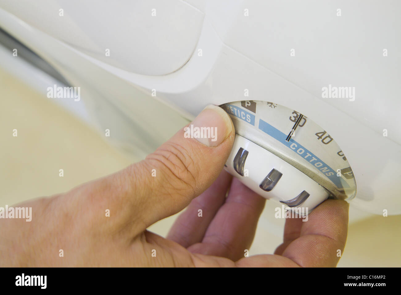 A person setting the dial of a washing machine to 30 degrees Stock Photo