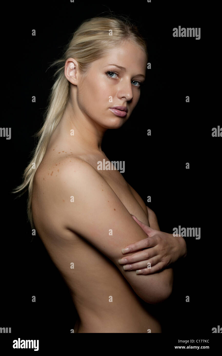 Young blond woman with bare upper body covering her breast with her arms Stock Photo