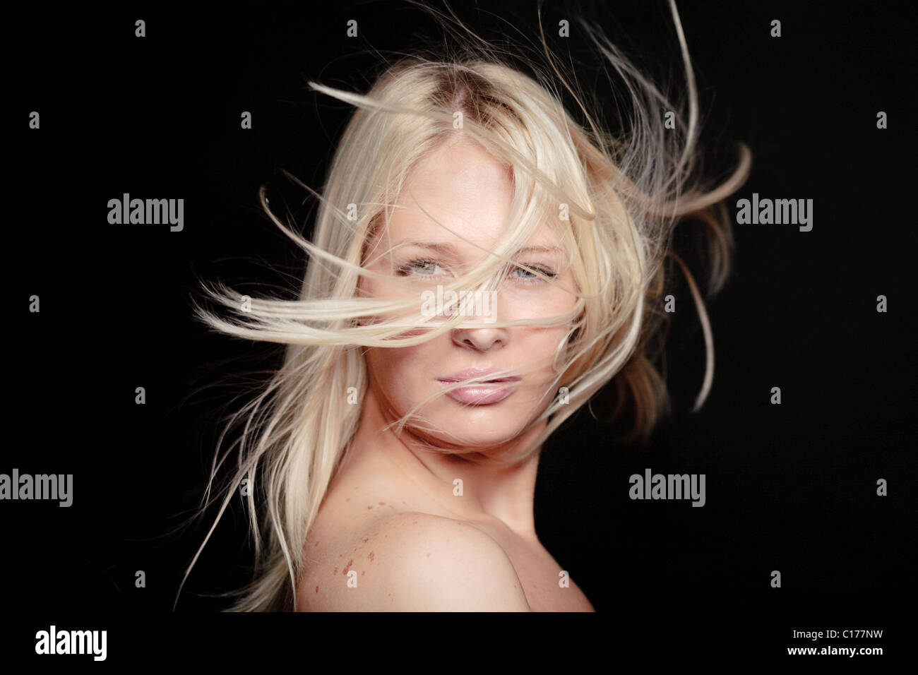 Portrait of a young blond woman with blowing hair in front of black screen Stock Photo