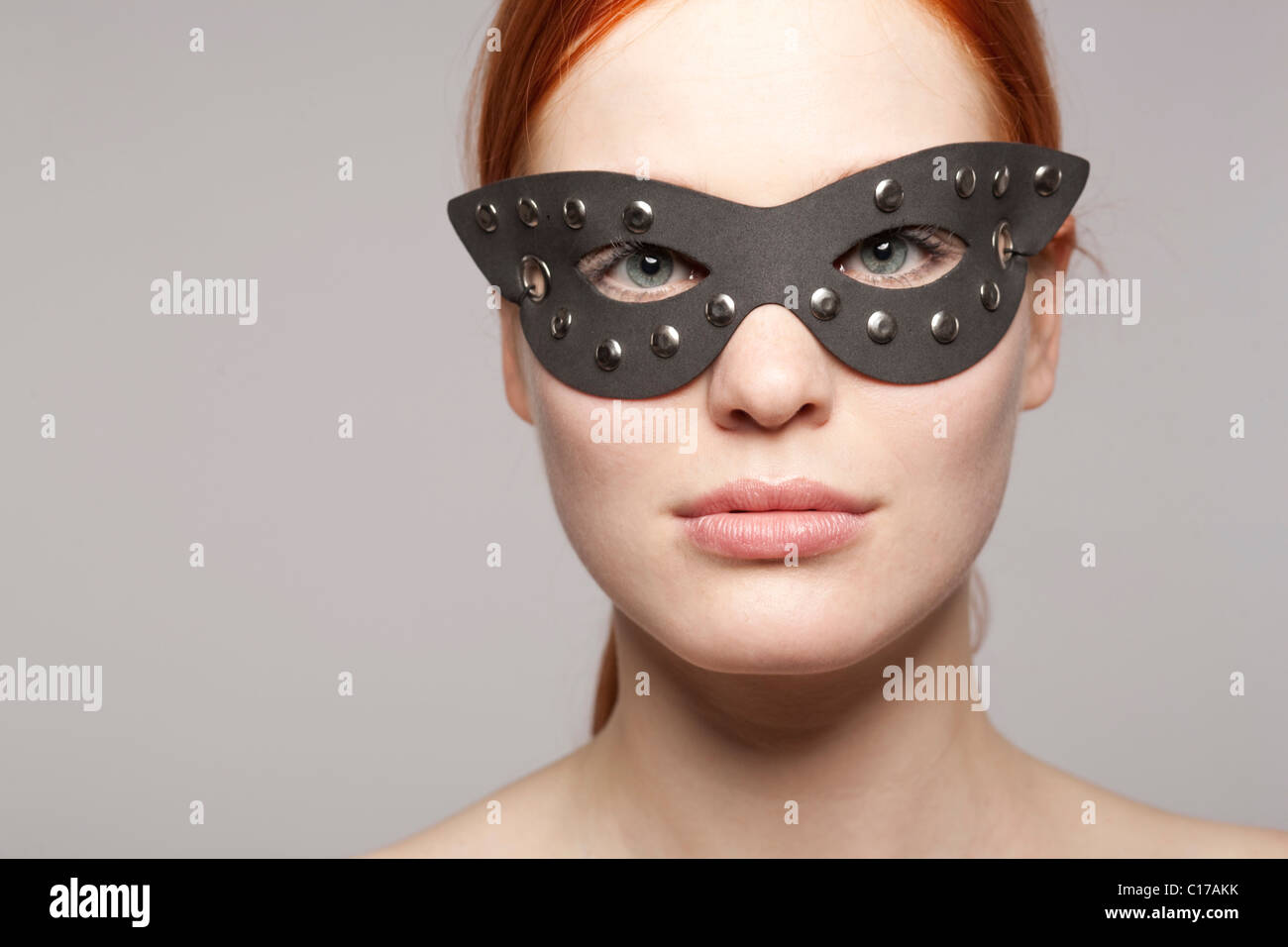 Young red-haired woman wearing a black leather mask Stock Photo
