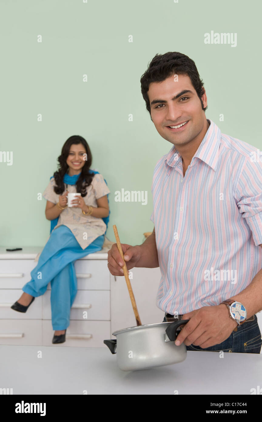 Man cooking with his wife drinking a cup of coffee in kitchen Stock Photo