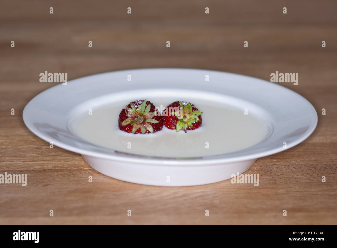 White saucer with fresh strawberries in milk with sugar poured over. Placed on wooden table Stock Photo