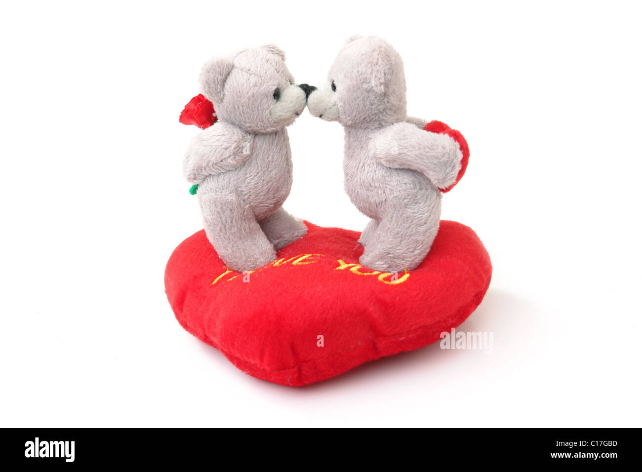 Two stuffed teddy bears kissing each other on stuffed heart-shaped pillow over white background Stock Photo