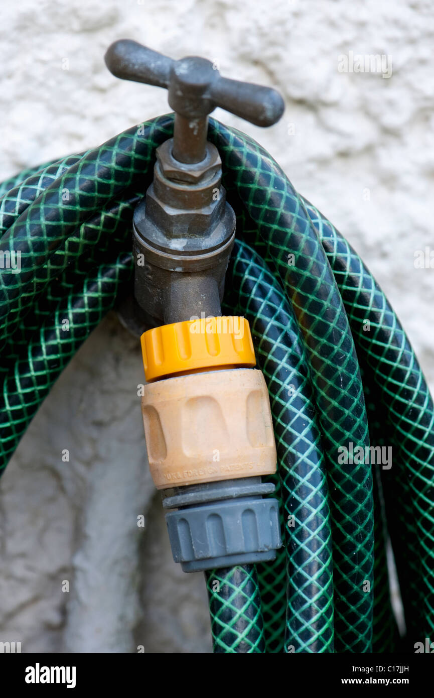 Old garden tap with plastic hose pipe attachment and hosepipe coiled. Stock Photo