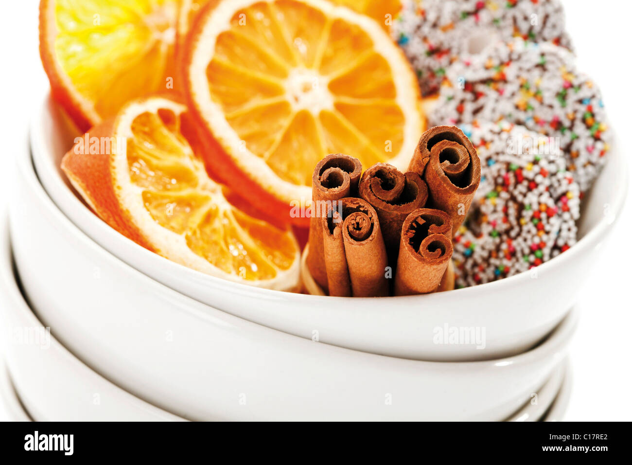 Dried organge slices with cinnammon sticks and chocolate rings in heap of white bowls, close-up Stock Photo