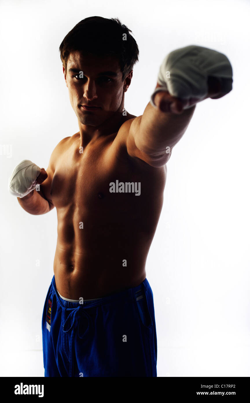 Young fighter with bare upper body and bandaged hands punching toward the camera, backlight Stock Photo