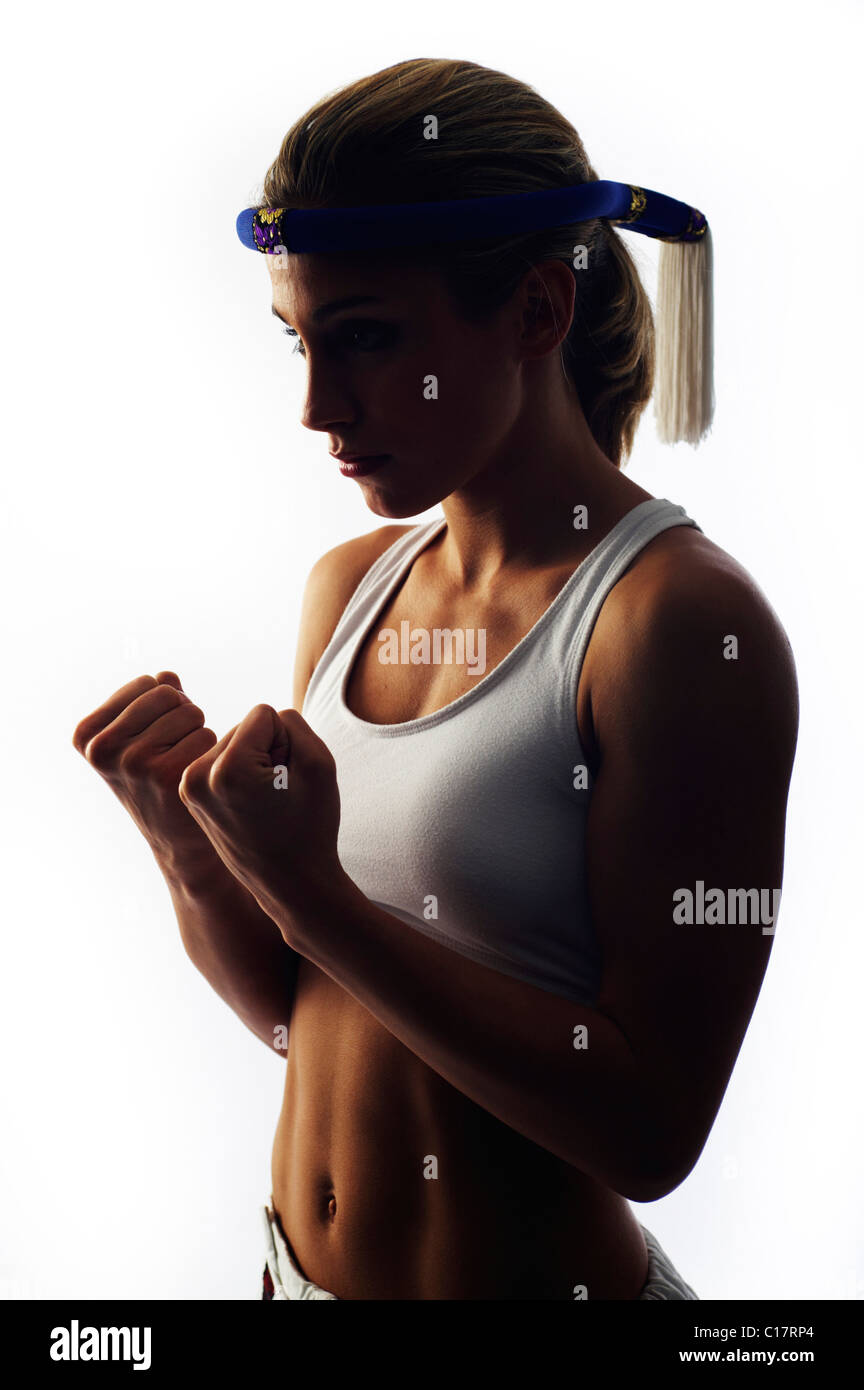 Young female fighter wearing a traditional Thai headband balling her fists, backlight Stock Photo