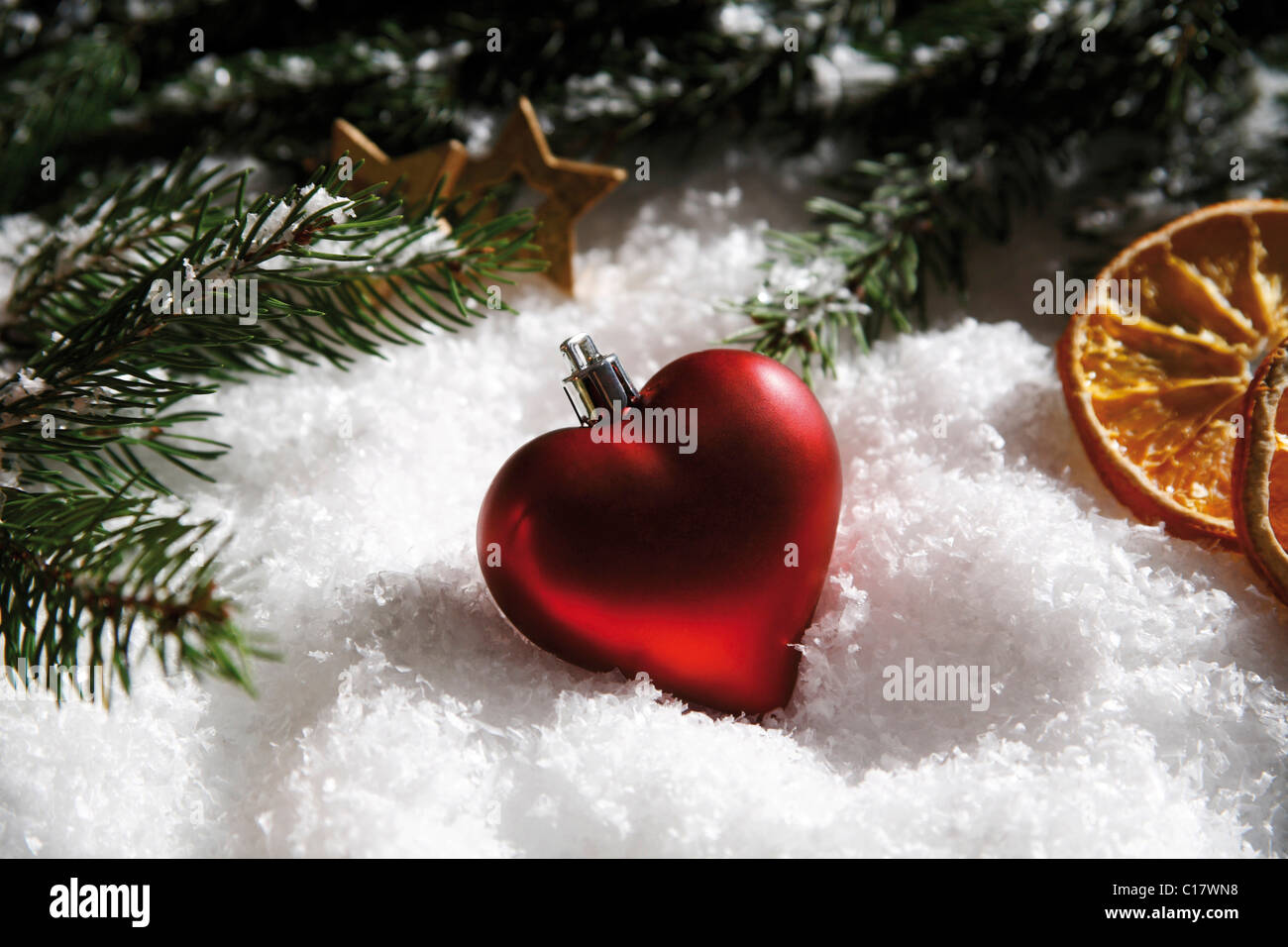Heart-shaped Christmas tree bauble, branches of fir, dried orange slices and decorations on snow Stock Photo