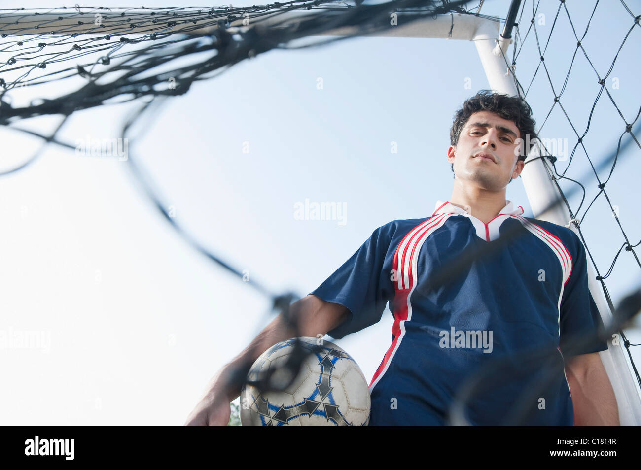 Soccer player holding a soccer ball behind the net Stock Photo