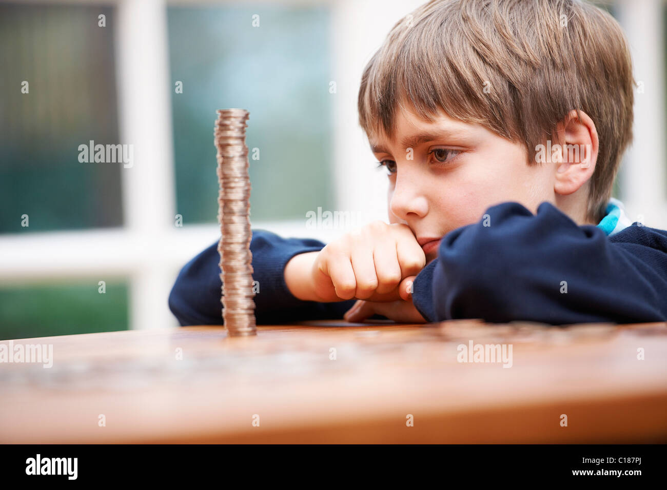 Boy looking at a tower of coins Stock Photo