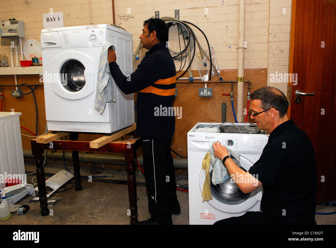 Men cleaning down recycled washing machines for resale, Clacton, Essex