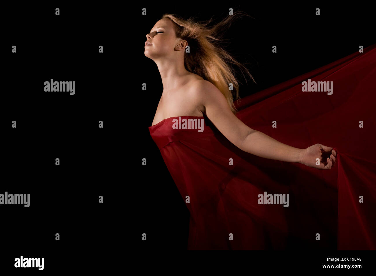 Young blonde woman wrapped in red cloth in front of a black backdrop Stock Photo