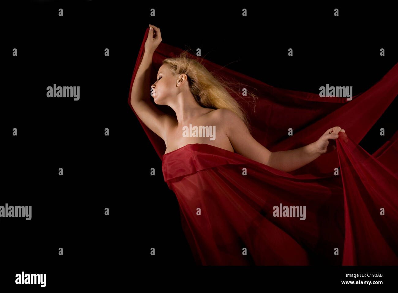 Young blonde woman wrapped in red cloth in front of a black backdrop Stock Photo
