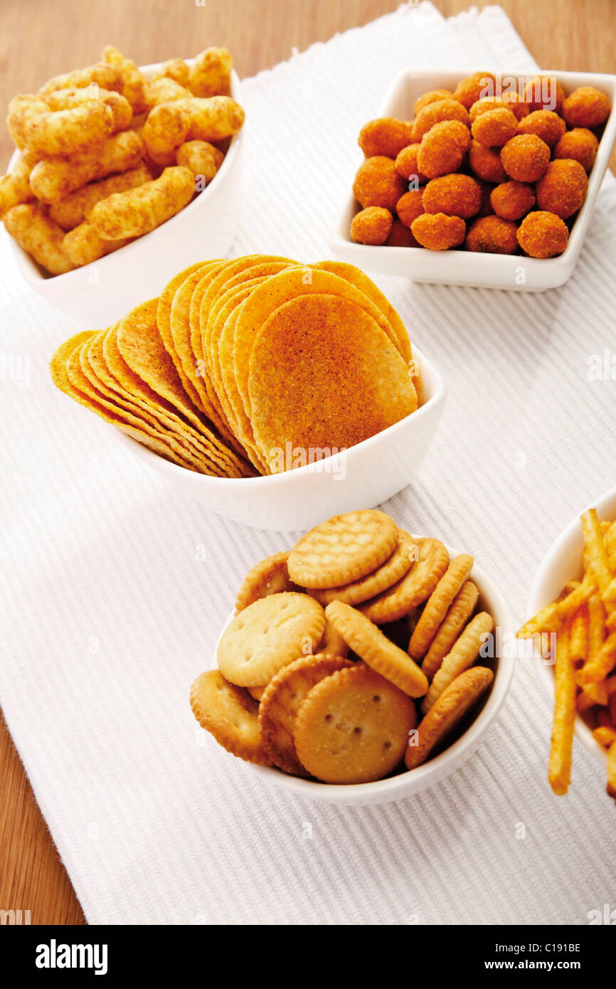 Various spiced snacks in bowls on a table, crisps, peanut flips, potato sticks and salted cookies Stock Photo