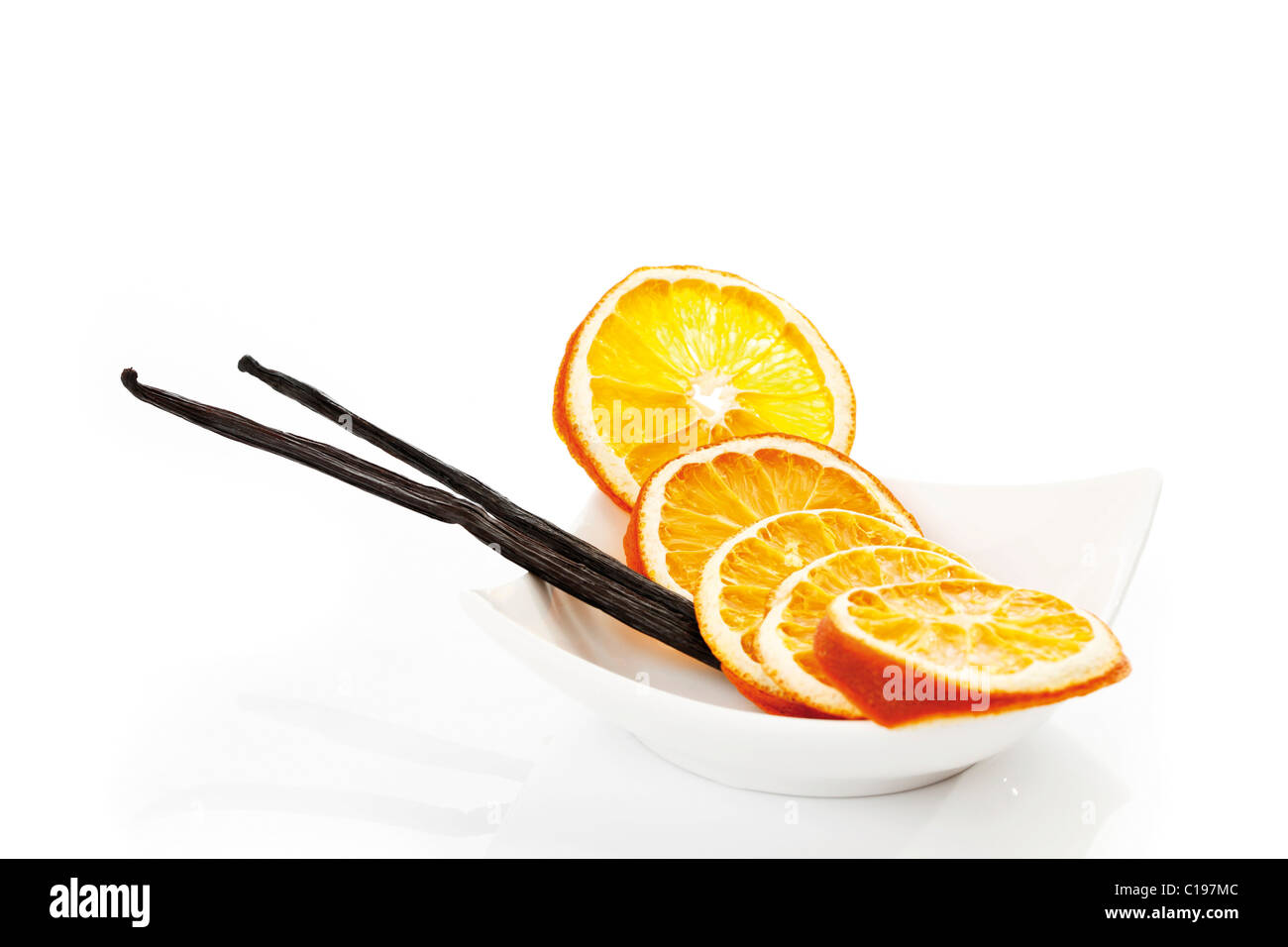 Dried slices of orange and vanilla sticks in a white bowl Stock Photo