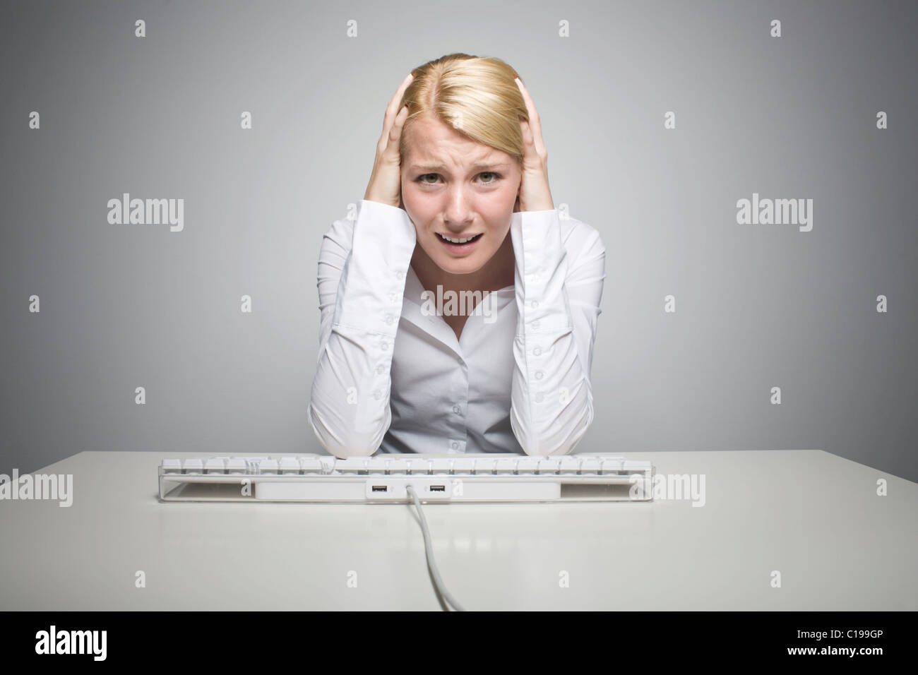 Young blond woman sitting in front of a computer keyboard, desperate Stock Photo