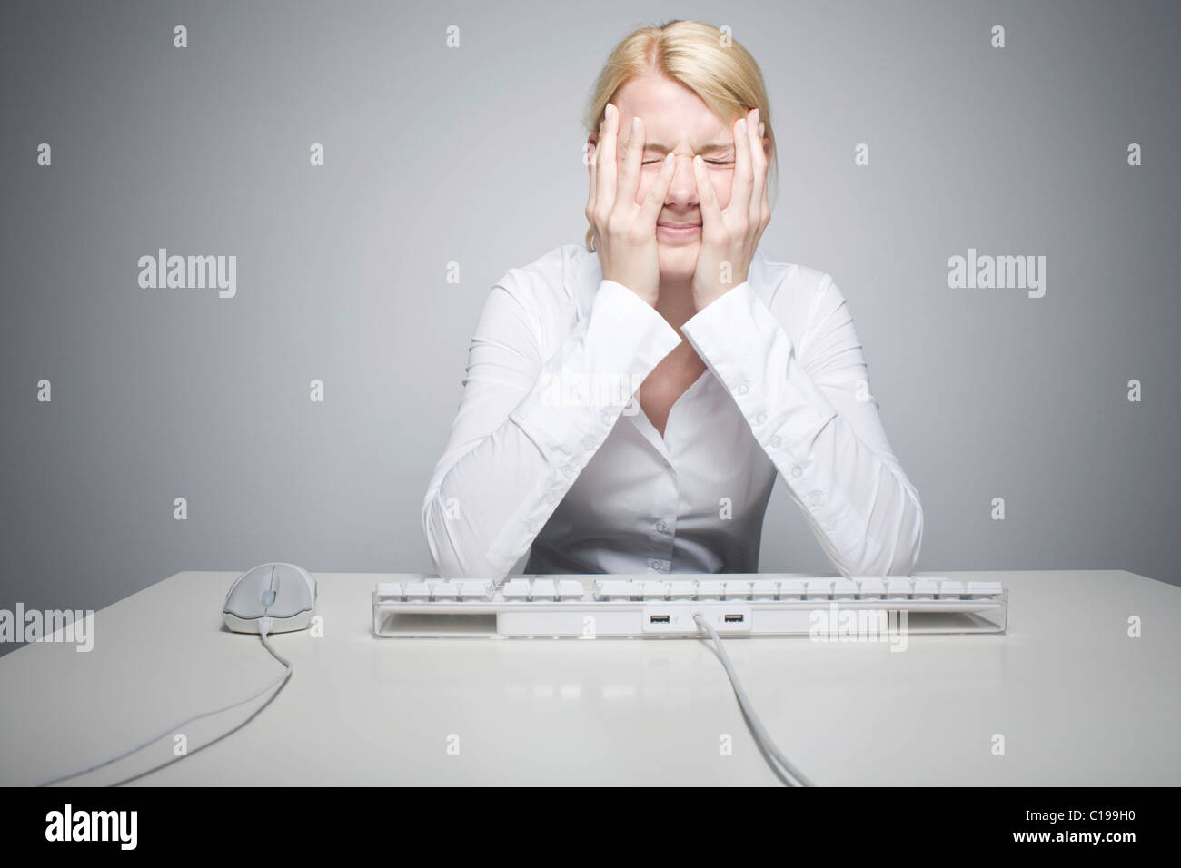 Young blond woman sitting in front of a computer keyboard, desperate Stock Photo