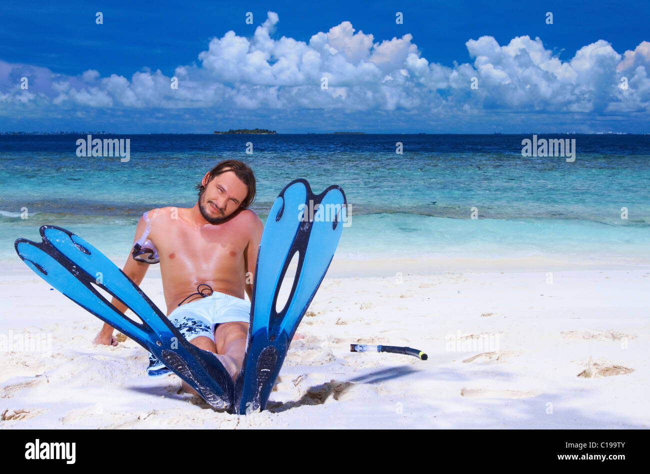 Handsome man is sitting on the beach wearing fin Stock Photo